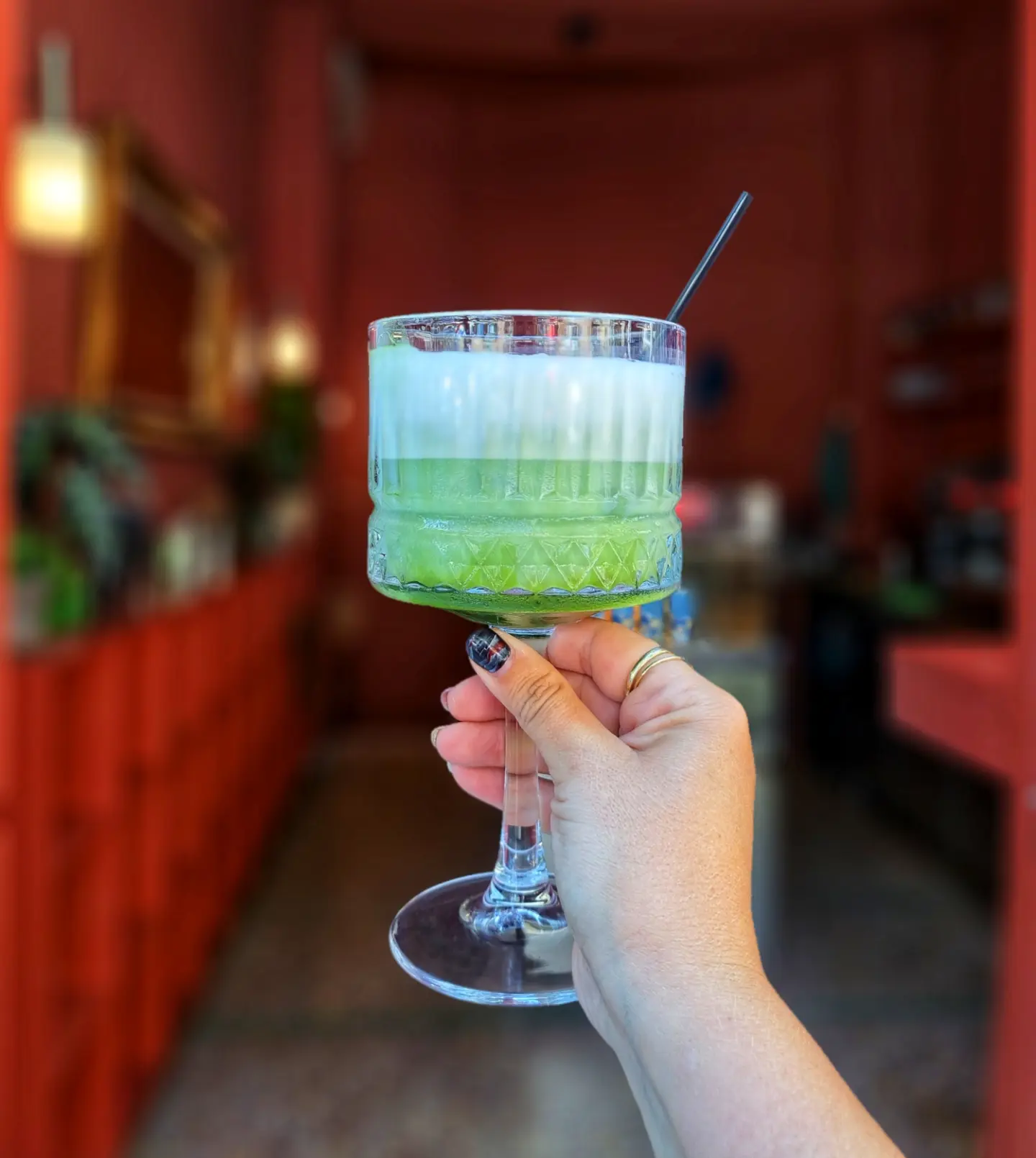 A hand holding an iced matcha in a coupe glass